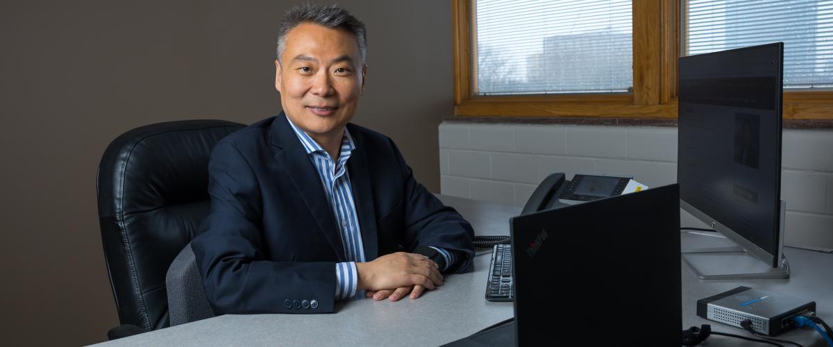 Photo of person sitting at desk with computers, smiling at camera