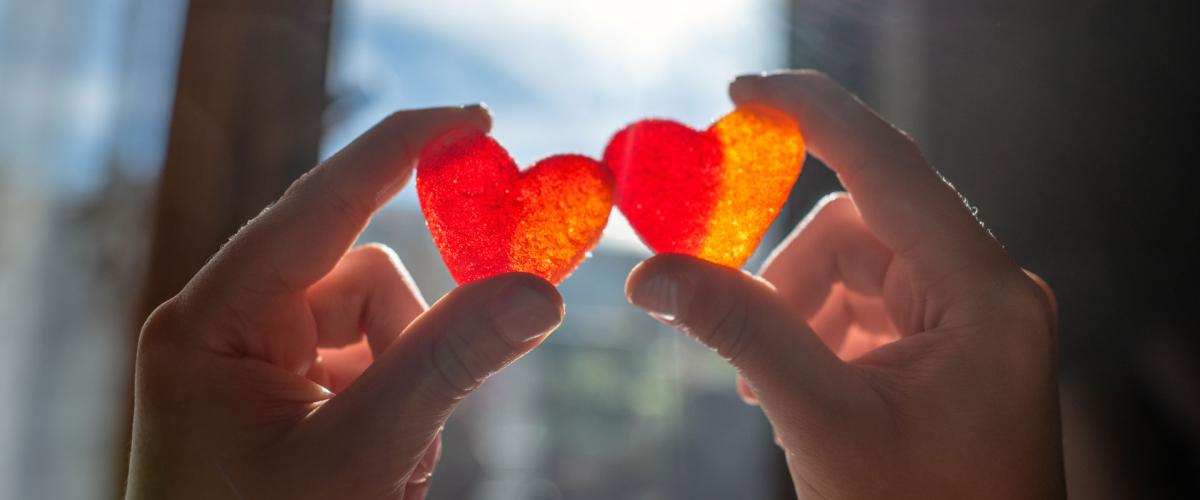 Photo of two people holding up candy hearts with sun shining through a window behind them