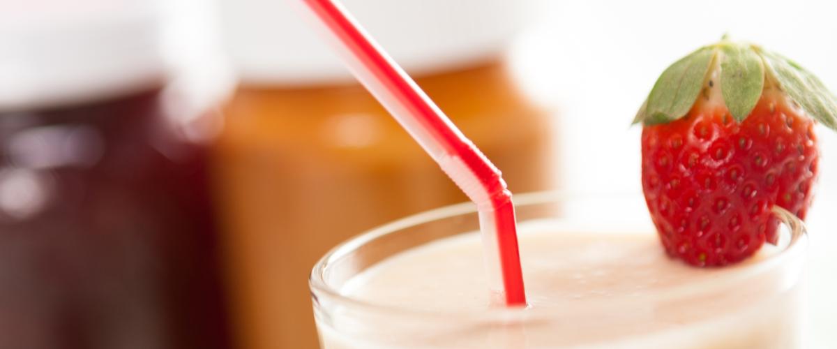 Close up of a smoothie with peanut butter and jelly jars in the background.