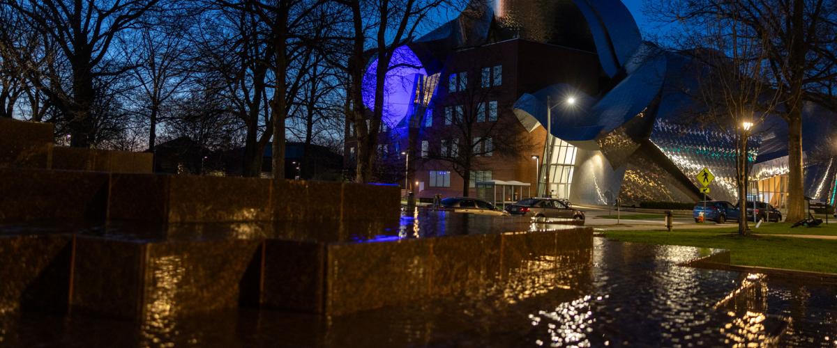 Photo of the Peter B. Lewis Building at night with lights reflecting off it and the water in the Merging sculpture in the foreground