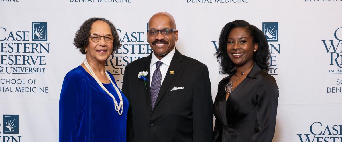 Three dental alumni award dinners pose in front of Case Western Reserve School of Dental Medicine logos after receiving their honors.