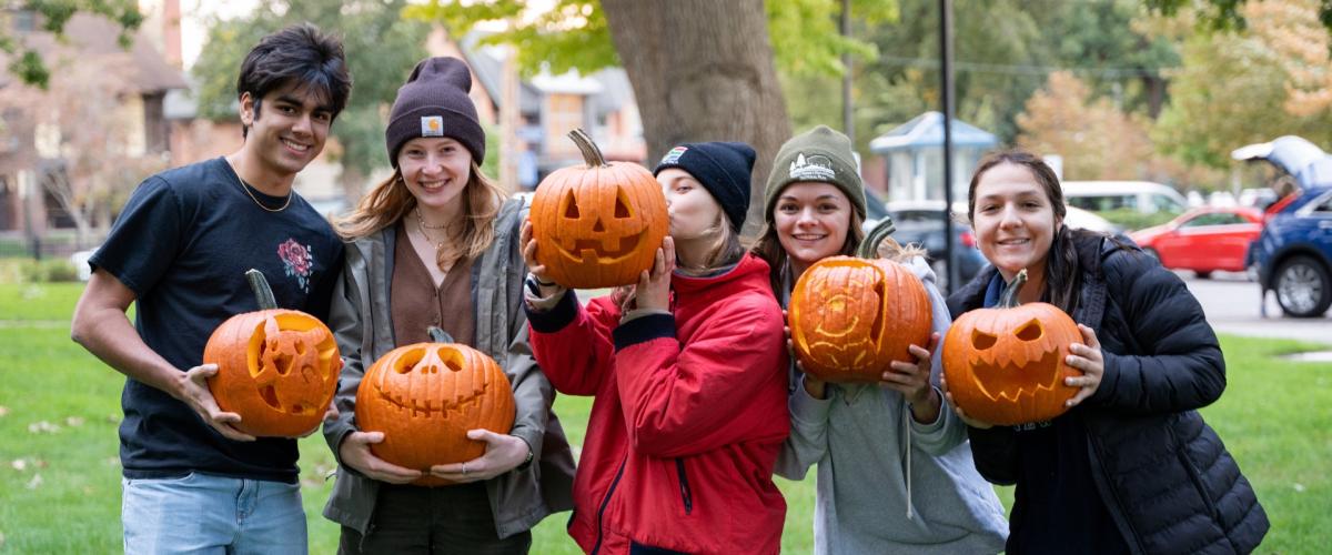 A group of happy students hold jack-o-lanterns. 