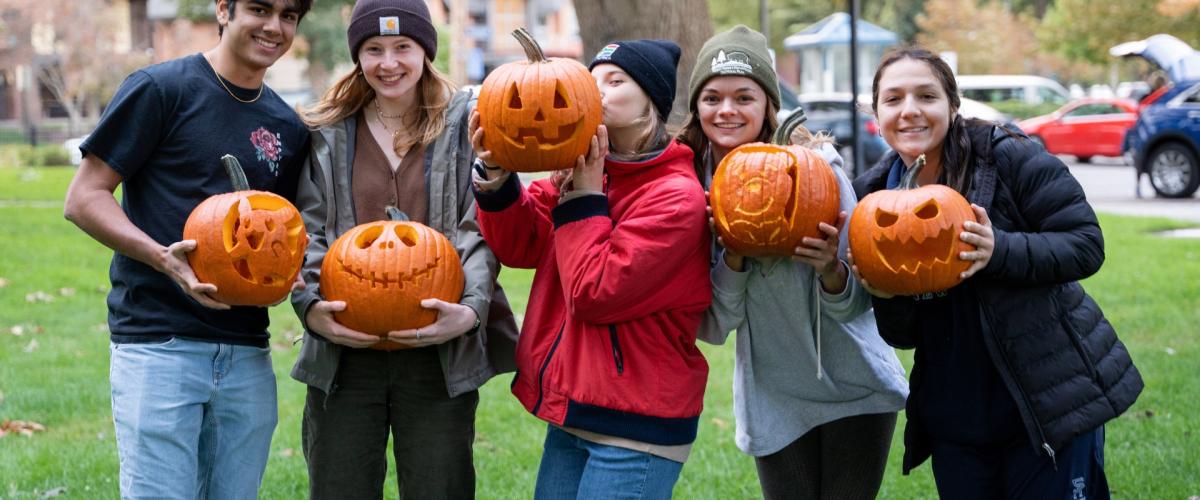 A group of happy students hold jack-o-lanterns. 