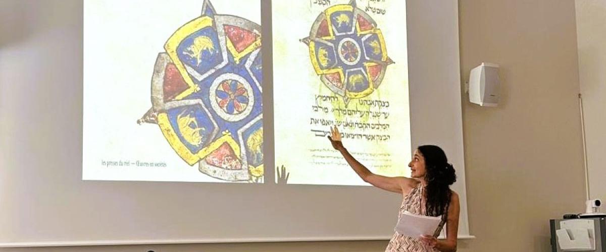 Photo of Elina Gertsman presenting at a symposium with the cover of her book on abstraction in medieval art projecting on the wall