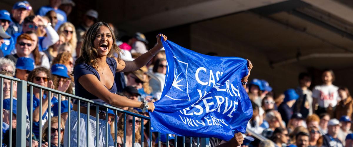 Excited member of the CWRU community holds a CWRU flag at a football game during Homecoming and Reunion weekend. 