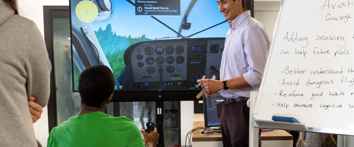 Photo of a PhD leading a demonstration of an aviation haptics program for a high school student
