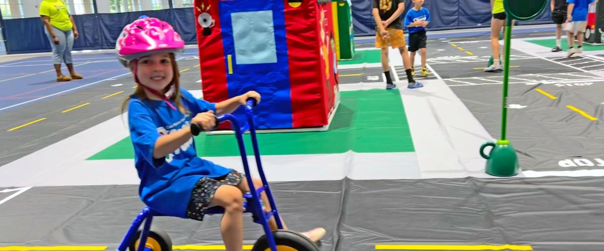 Photo of a child wearing a helmet riding a tricycle on a model town set up for CWRU's Safety Town