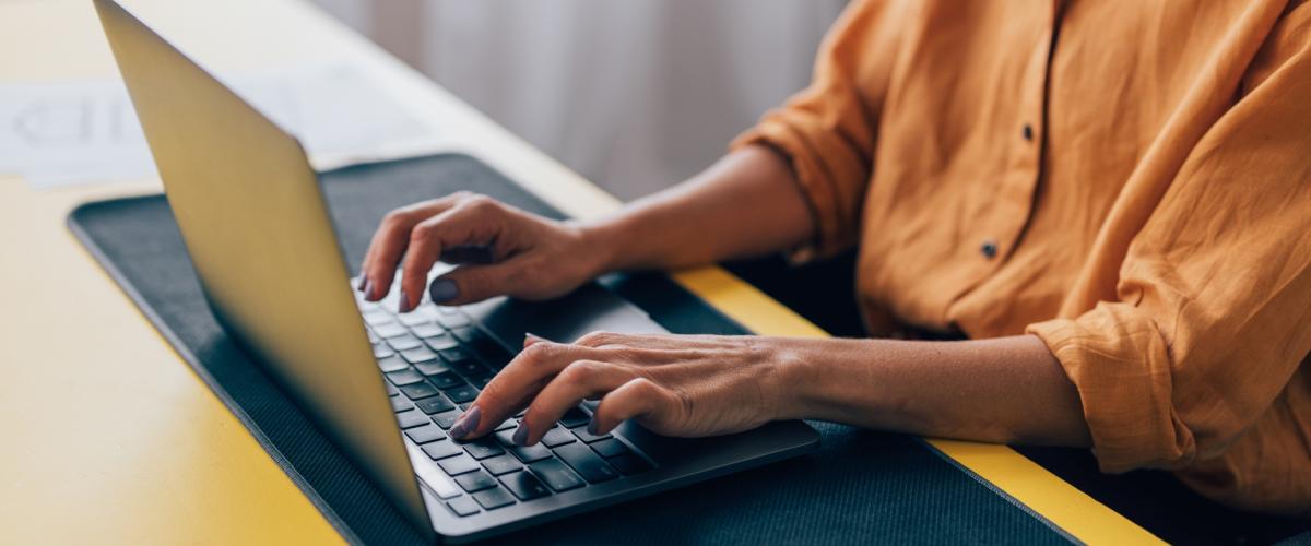 Close up of an individual typing on a laptop at a desk.