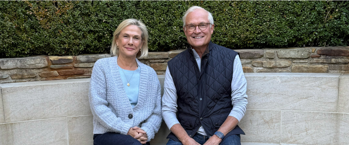 Lady in a blue sweater sitting next to a man with a vest outside 