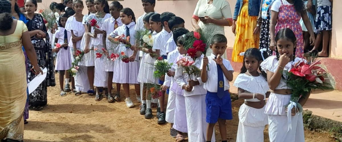 Village children of Boralanda standing in front of a building holding flowers