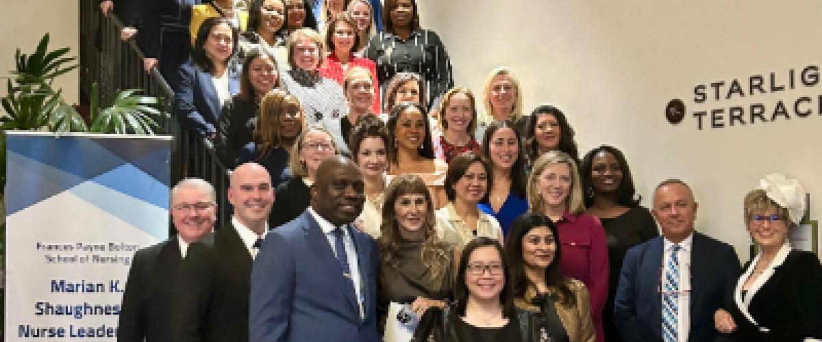 A large group of people poses on a staircase by a sign for the arian K. Shaughnessy Nurse Leadership Academy. 