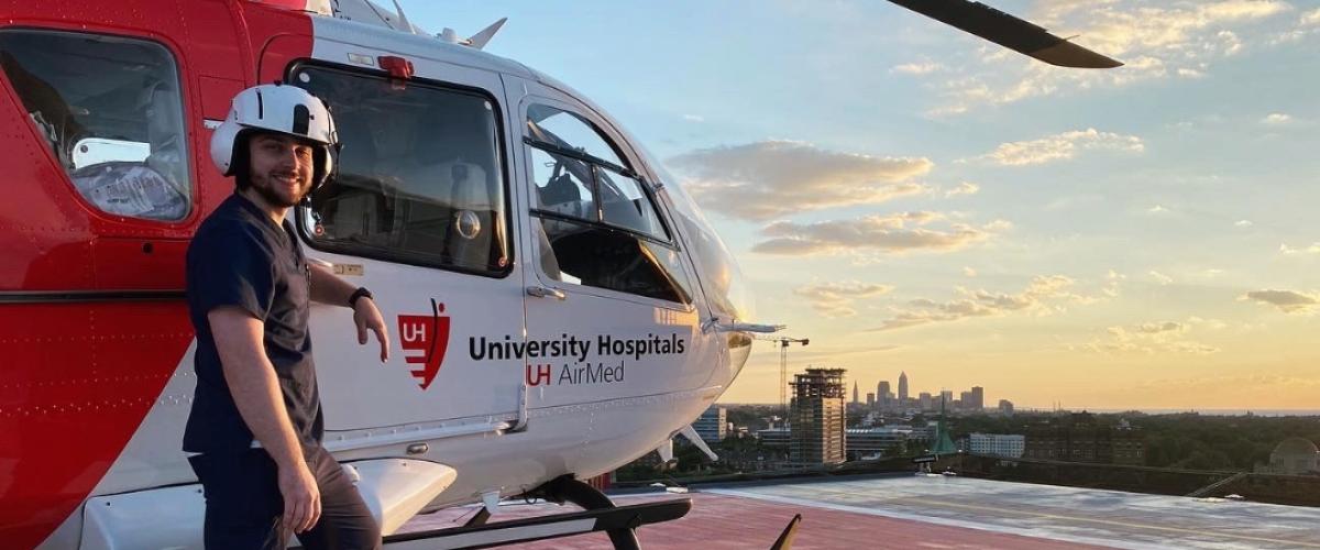 CRNA student Robert Sharkey stands in front of a medical helicopter on a rooftop.