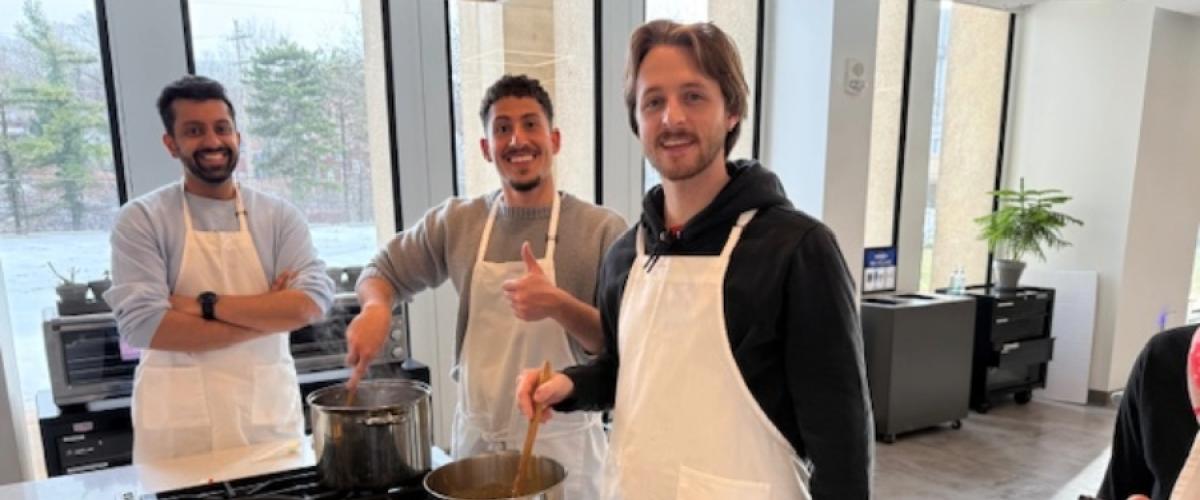 three students smiling together while cooking in the teaching kitchen