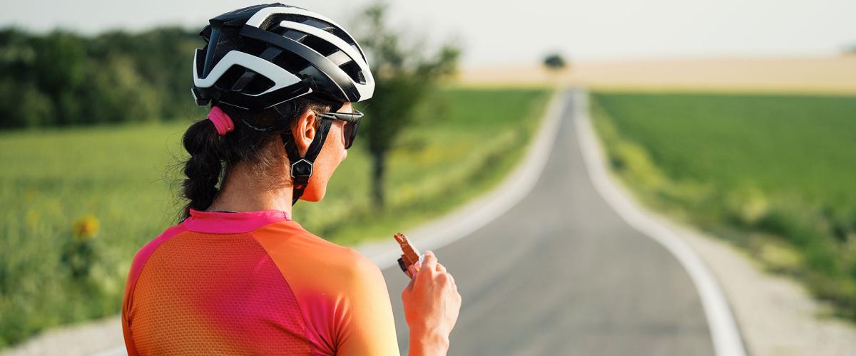 Photo from behind of a cyclist eating a protein bar while taking a break on the road