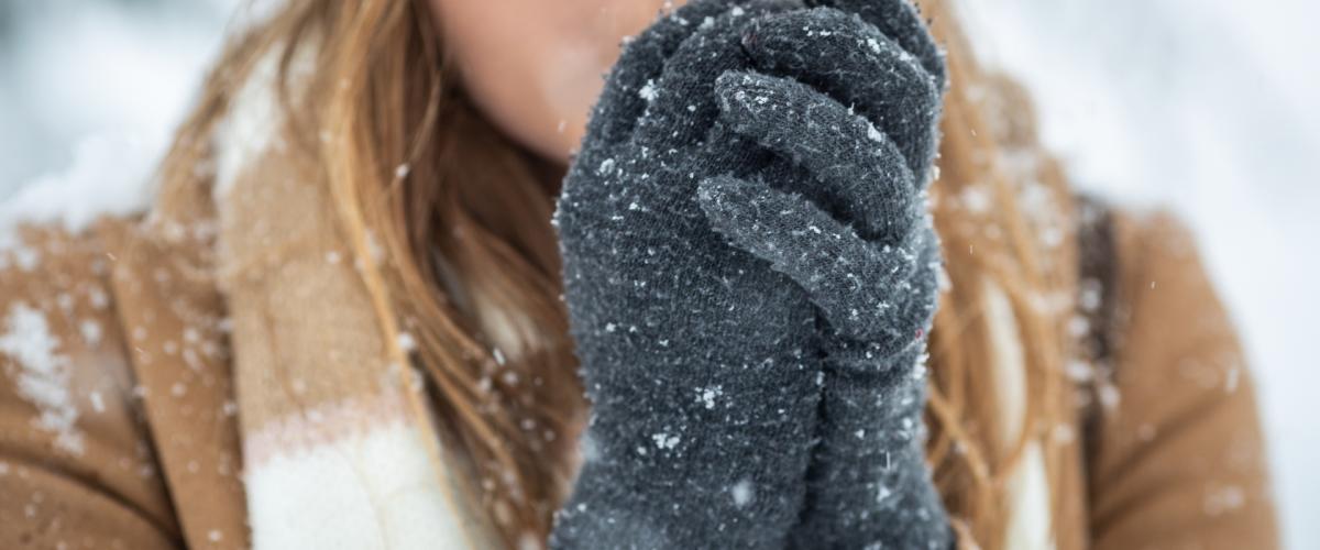 Close up of a woman blowing on her hands to warm them in the cold weather.