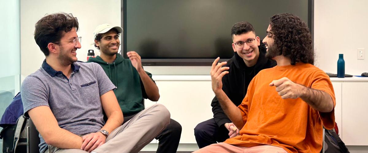 four medical students sitting in chairs, laughing with each other as they act out an improv sketch