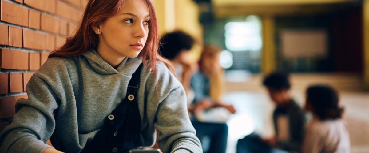 Girl sitting in school hallway holding phone with other kids in the background