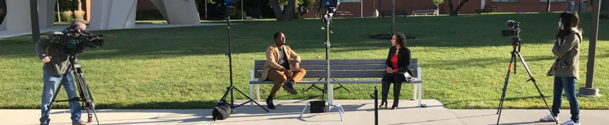 A member of the CWRU community being interviewed outdoors while sitting on a bench.
