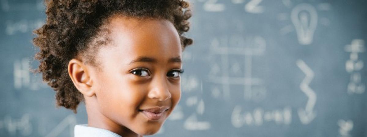Girl looks back and smiles in front of a chalkboard with math problems on it