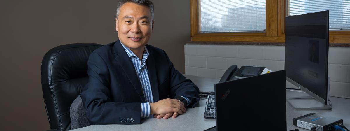 Photo of person sitting at desk with computers, smiling at camera