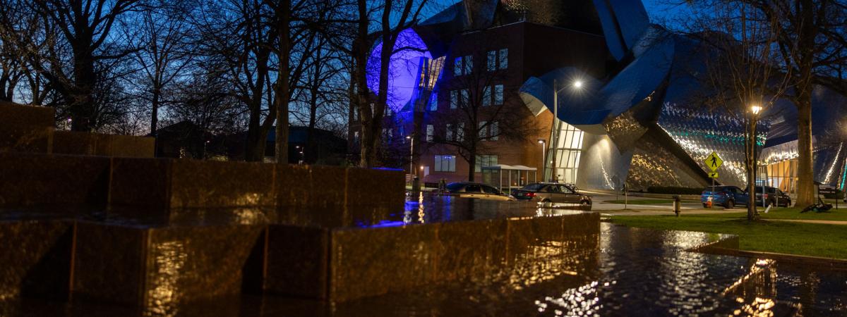 Photo of the Peter B. Lewis Building at night with lights reflecting off it and the water in the Merging sculpture in the foreground