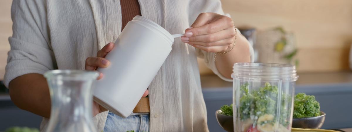 Close up photo of a woman adding protein powder to a smoothie