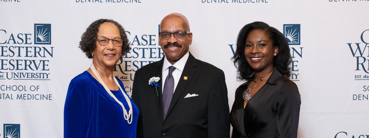 Three dental alumni award dinners pose in front of Case Western Reserve School of Dental Medicine logos after receiving their honors.