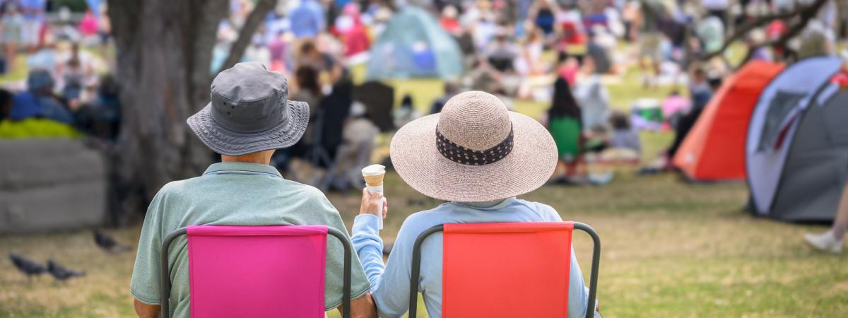 Photo of an elderly couple sitting next to one another in lawn chairs at an outdoor event