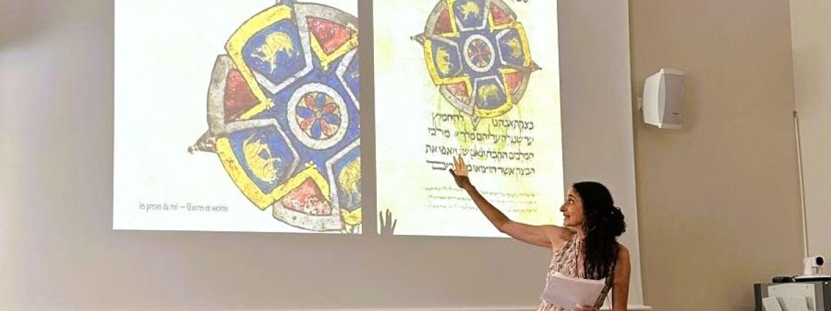 Photo of Elina Gertsman presenting at a symposium with the cover of her book on abstraction in medieval art projecting on the wall
