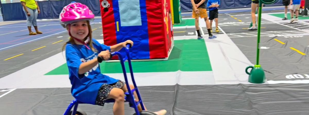 Photo of a child wearing a helmet riding a tricycle on a model town set up for CWRU's Safety Town