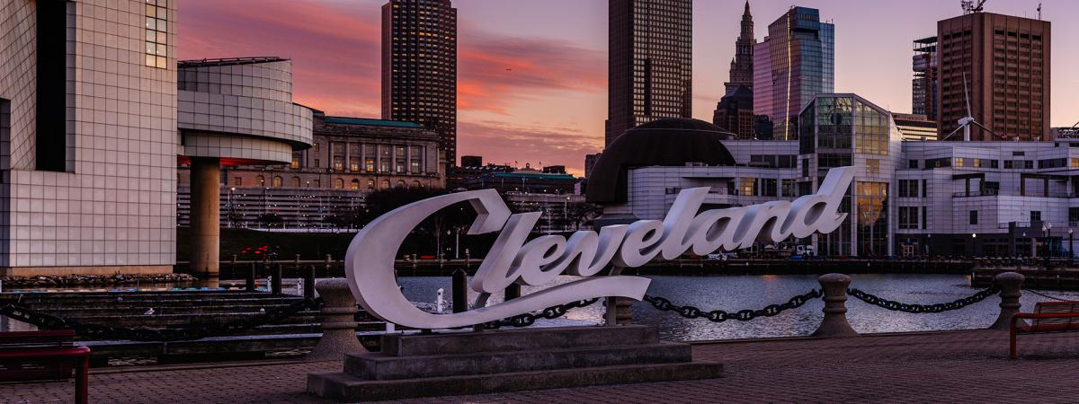 Photo of the Cleveland script sign in front of the Rock and Roll Hall of Fame with the city skyline in the background at dusk