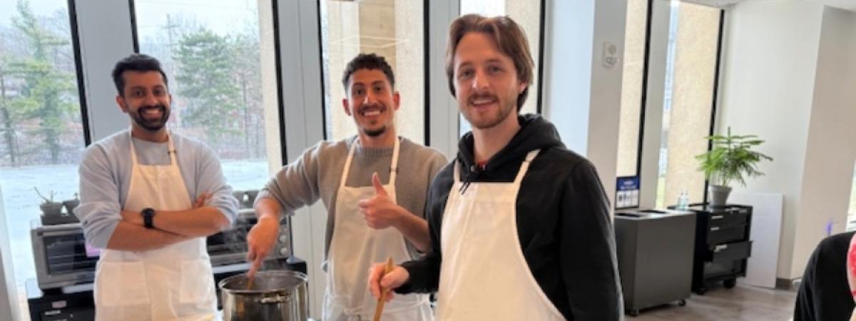 three students smiling together while cooking in the teaching kitchen
