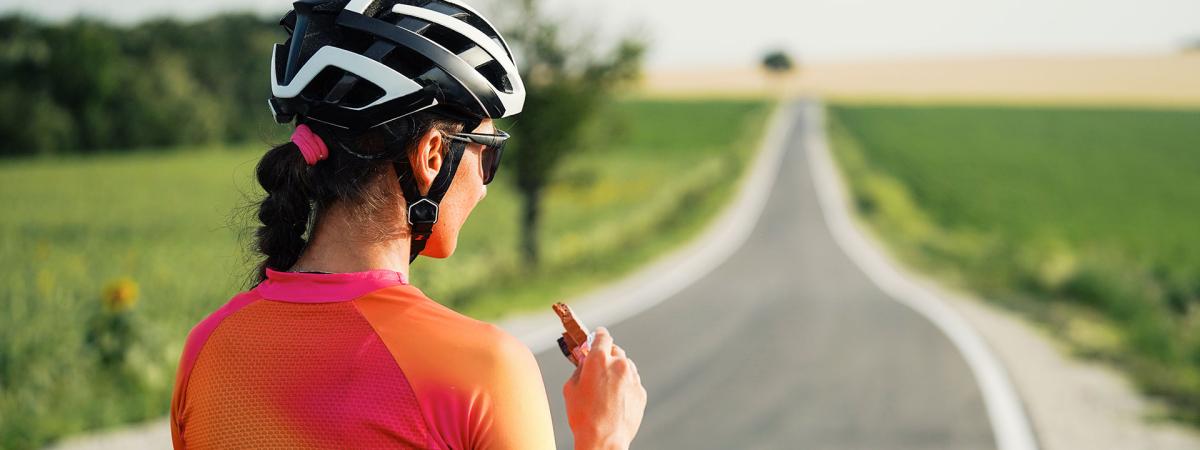 Photo from behind of a cyclist eating a protein bar while taking a break on the road
