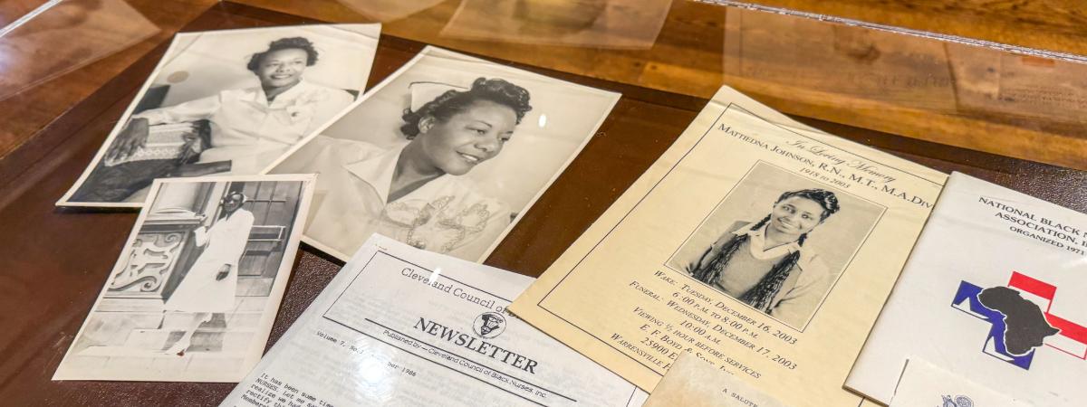A selection of papers feature photos of Black nurses are spread out in a display case.