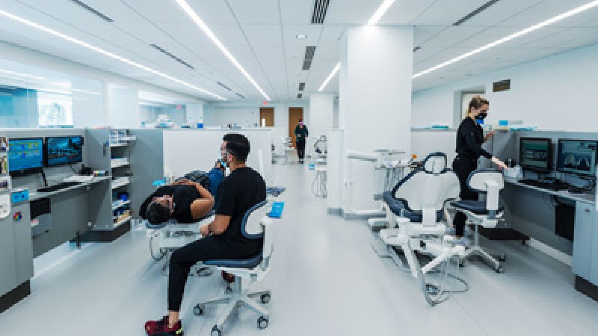 A modern dental clinic with sleek white interiors and several patients receiving care. Dentists and staff, wearing black uniforms and masks, attend to patients in dental chairs.