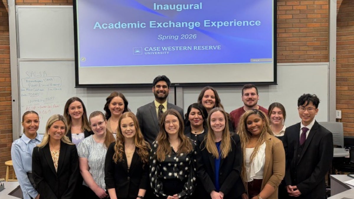 Group of students standing in front of a screen that says "Inaugural Academic Exchange Experience Spring 2026"