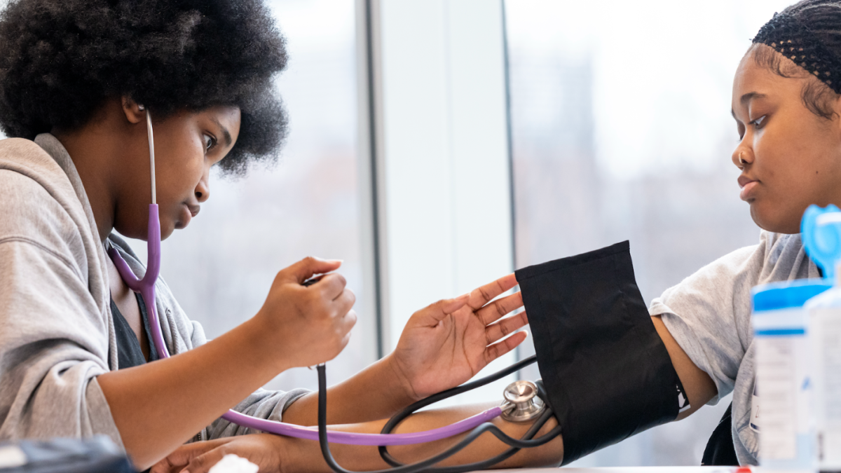 A student wearing a stethoscope checks the blood pressure on another student.