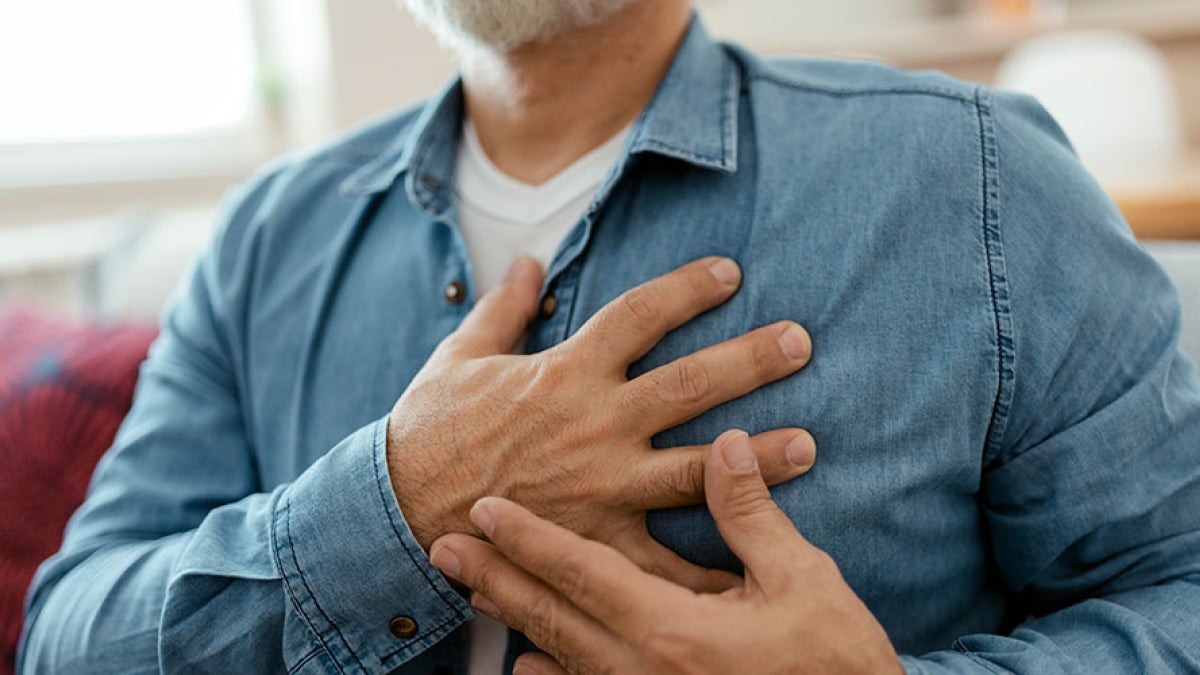 Close up photo of a man clutching his chest over his heart with both hands