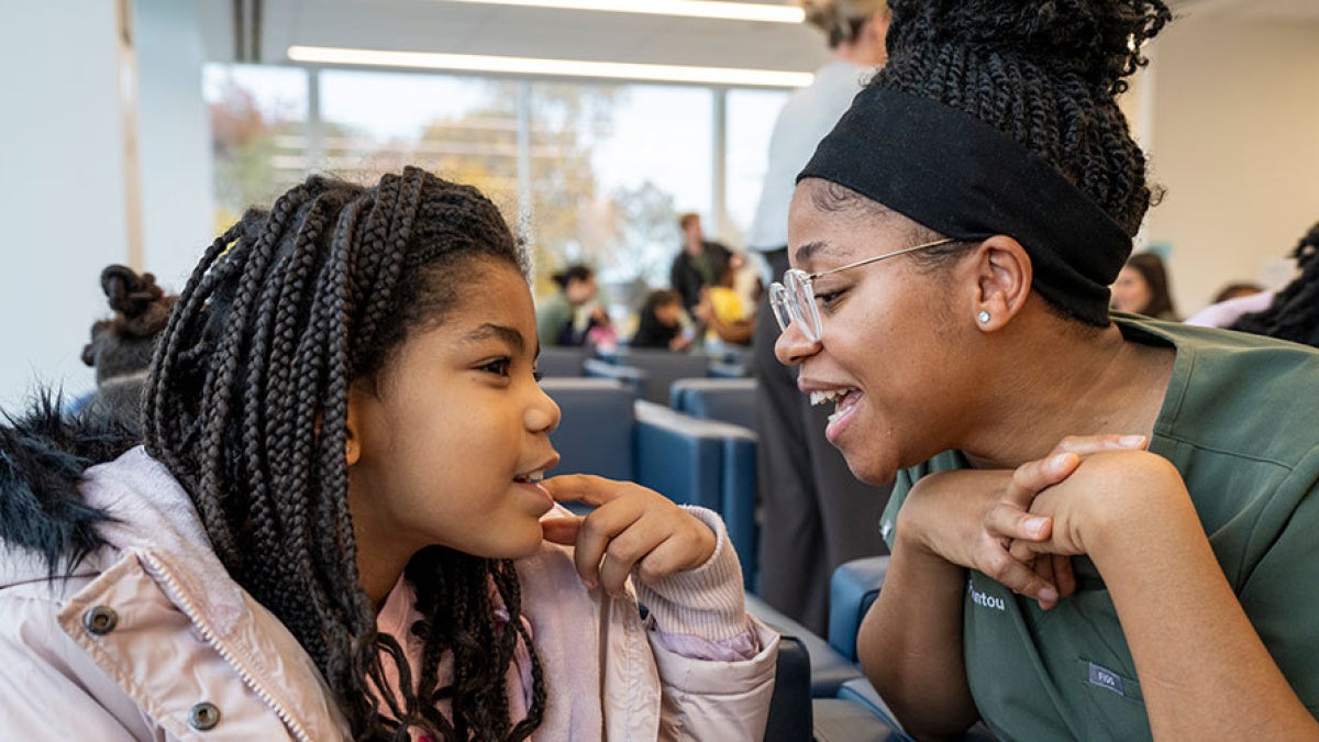 A child points to one of her teeth while a CWRU dental medicine student takes a look in the dental clinic waiting area