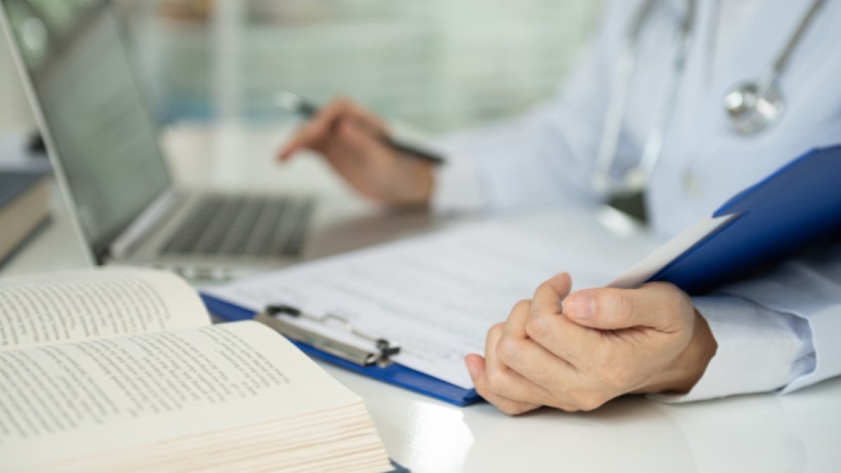 An unidentified person wearing a stethoscope writes in a book