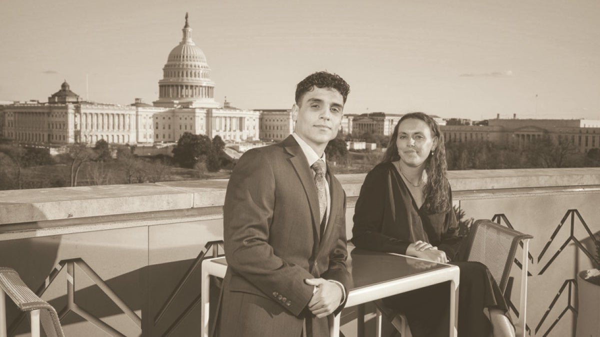 Felipe Joglar-Viera and Shannon Moore in formal attire sit at an outdoor table, with the U.S. Capitol in the background. 