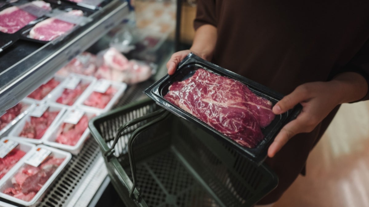 Hands hold raw meat package at a grocery store 