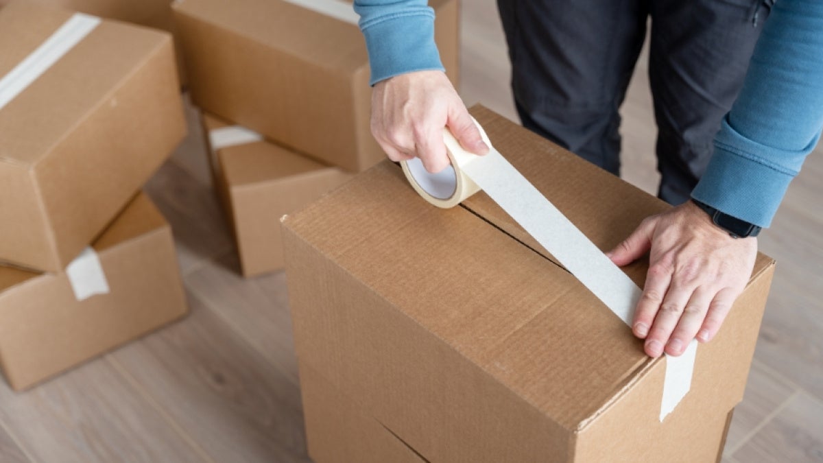 Close up of a person wrapping a moving box with masking tape. 