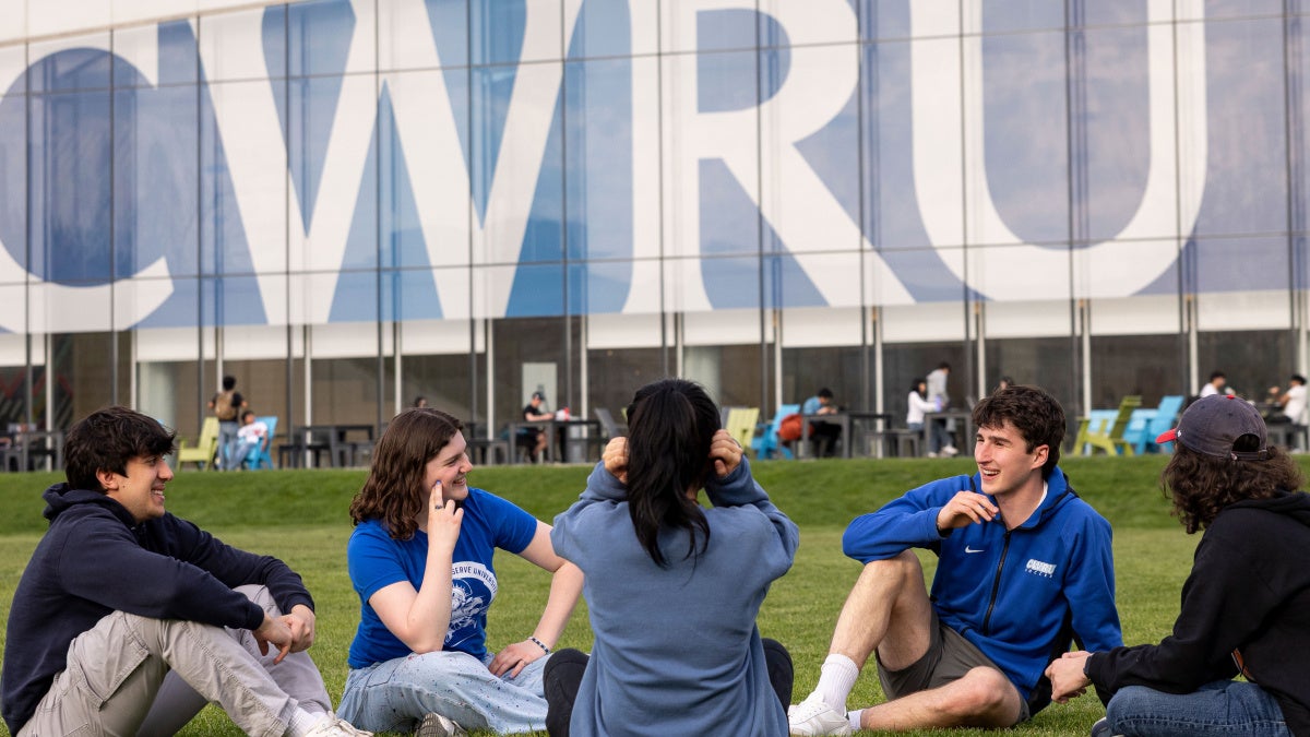 Five students sit in front of large “CWRU” signage on Freiberger Field.