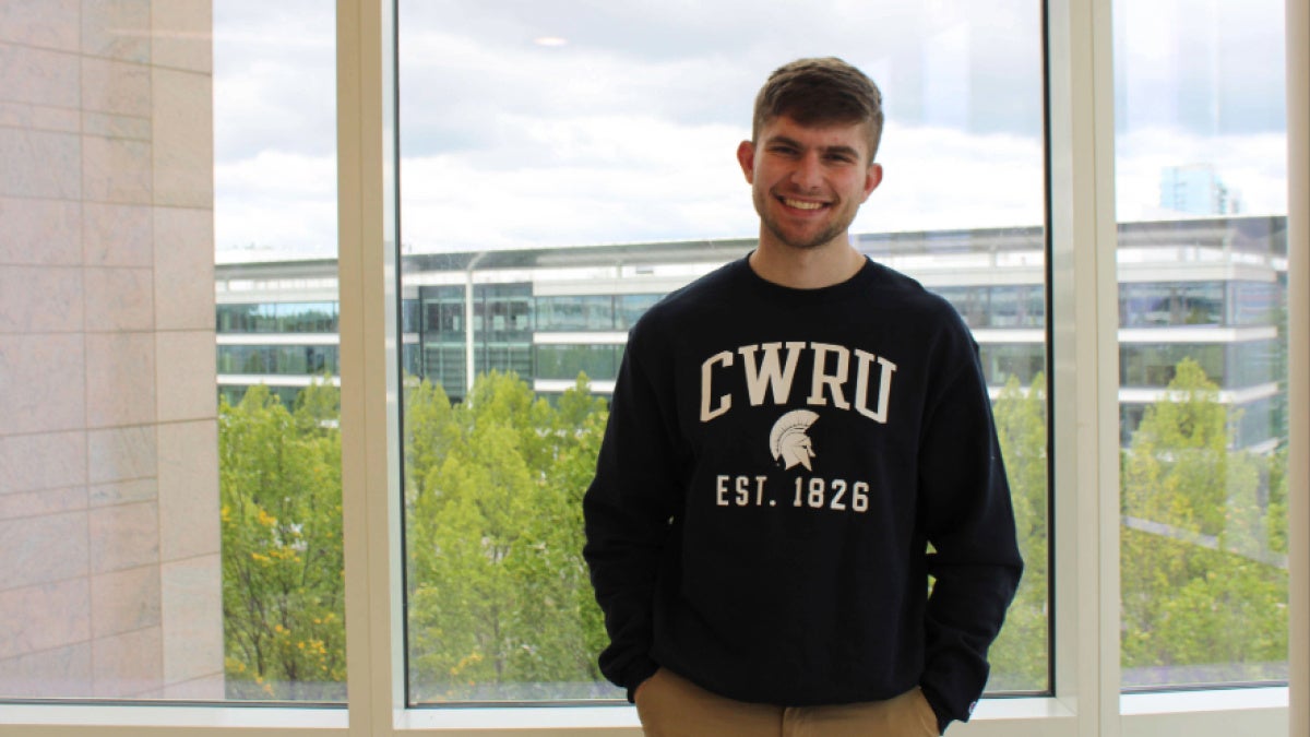 Jacob Hoffa stands in front of a window in front of Samson Pavilion wearing a CWRU sweatshirt.