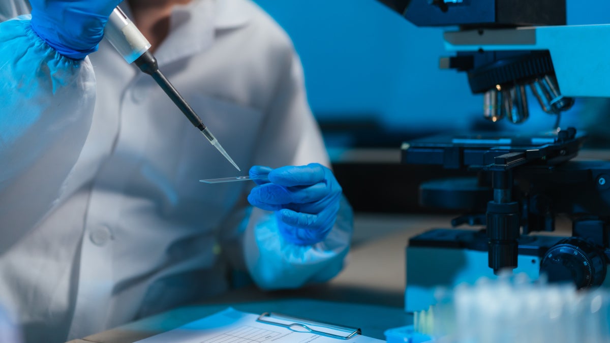 Photo of lab researcher with microscope and slide.