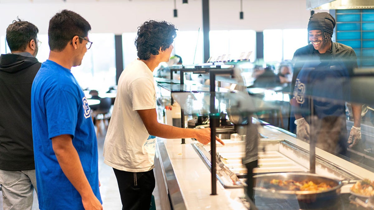 Students at the counter of a CWRU dining hall as a smiling employee prepares to serve them food