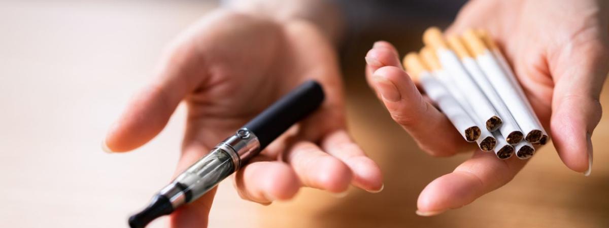 Hand Holding Vape And Tobacco Cigarettes Over Wooden Desk