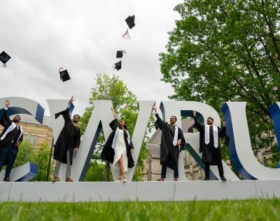 Five students stand in front of the CWRU sign and throw their commencement hats in the air