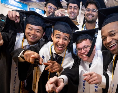 A group of students stand together in commencement regalia for a fun photo